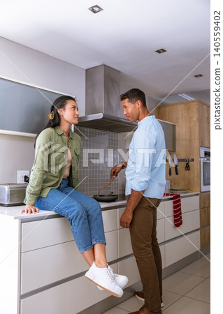 Asian couple chatting and cooking breakfast in modern home kitchen with frying pan Asian couple chatting and cooking breakfast in modern home kitchen with frying pan 140559402