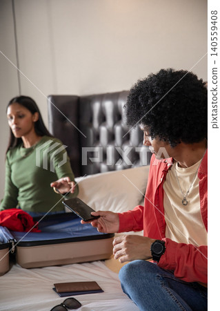 Diverse couple packing suitcase on bed in bedroom, holding smartphone, passport, sunglasses Diverse couple packing suitcase on bed in bedroom, holding smartphone, passport, sunglasses 140559408