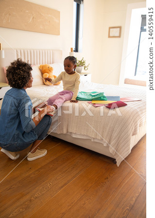Mother and african american daughter kneeling by bed tying sneaker laces next to backpack Mother and african american daughter kneeling by bed tying sneaker laces next to backpack 140559415