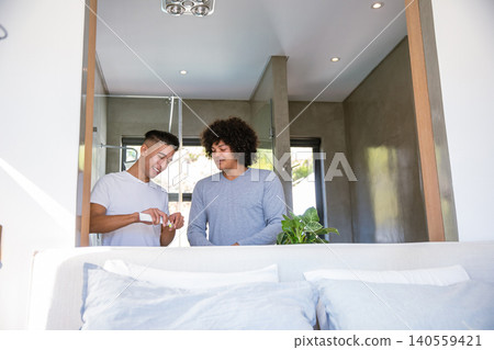 Diverse male friends applying lotion from tube onto hand in modern bedroom with potted plant Diverse male friends applying lotion from tube onto hand in modern bedroom with potted plant 140559421
