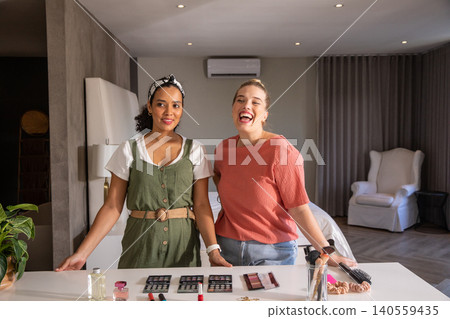 Diverse female friends arranging makeup brushes, palettes on bedroom counter with potted plant Diverse female friends arranging makeup brushes, palettes on bedroom counter with potted plant 140559435
