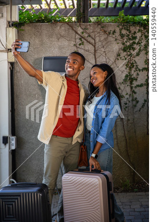 African American couple taking smartphone selfie under pergola on patio with luggage African American couple taking smartphone selfie under pergola on patio with luggage 140559440