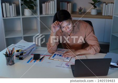 Asian man in 20s feeling stressed working late at home office Asian man in 20s feeling stressed working late at home office 140559483