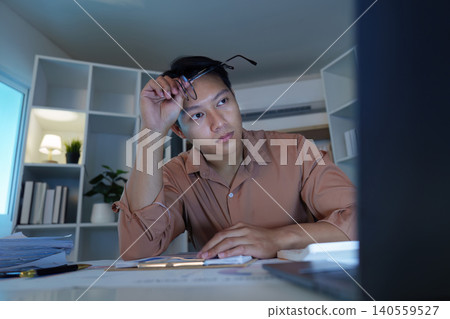 Asian man in his 20s working late at home office feeling stressed 140559527