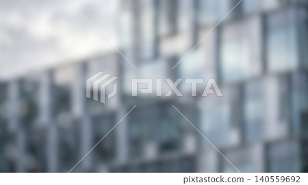 Abstract blurred modern corporate business glass office building exterior featuring repeating geometric square windows reflecting cloudy sky creating city architecture background 140559692