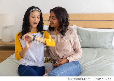 Diverse mother and daughter hugging while examining smartwatch and gift box in bedroom Diverse mother and daughter hugging while examining smartwatch and gift box in bedroom 140559736