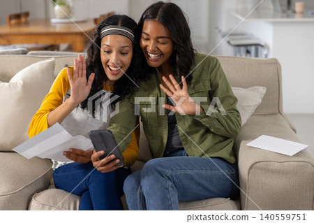 Diverse mom and teenage daughter holding smartphone while showing sheet of paper Diverse mom and teenage daughter holding smartphone while showing sheet of paper 140559751