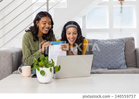 Diverse mom and teenage daughter reviewing letter from blue envelope on sofa at home Diverse mom and teenage daughter reviewing letter from blue envelope on sofa at home 140559757