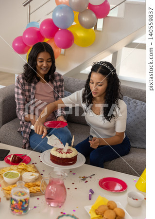Diverse mom and teenage daughter slicing red velvet cake with spatula in living room Diverse mom and teenage daughter slicing red velvet cake with spatula in living room 140559837