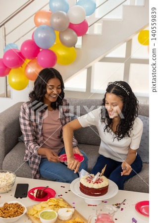 Diverse mom and teenage daughter serving red velvet cake with knife on couch Diverse mom and teenage daughter serving red velvet cake with knife on couch 140559839