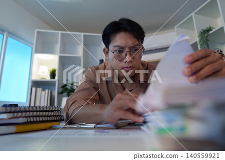 Asian man in his 20s working late at home office with documents 140559921