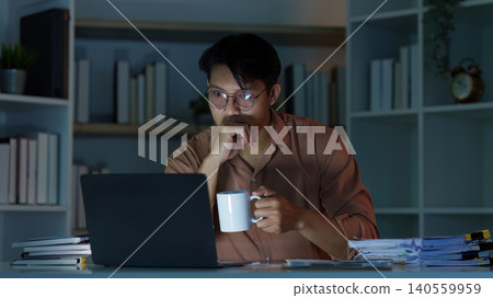 Asian man focused on remote work and productivity at home office at night Asian man focused on remote work and productivity at home office at night 140559959