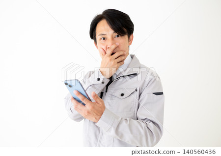 一位身穿灰色工作服的中年商人,在白色背景下看著他的智慧型手機,臉上露出震驚的表情。 一位身穿灰色工作服的中年商人,在白色背景下看著他的智慧型手機,臉上露出震驚的表情。 140560436