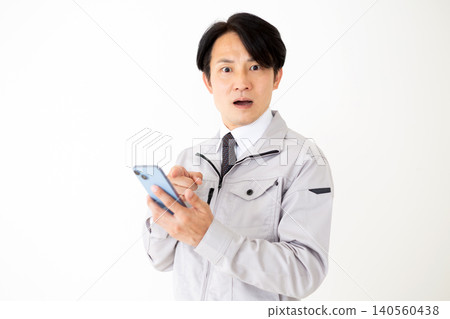 一位身穿灰色工作服的中年商人,在白色背景下看著他的智慧型手機,臉上露出震驚的表情。 一位身穿灰色工作服的中年商人,在白色背景下看著他的智慧型手機,臉上露出震驚的表情。 140560438