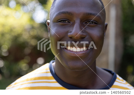 African american adult male smiling brightly while standing in backyard with sunlit foliage African american adult male smiling brightly while standing in backyard with sunlit foliage 140560502