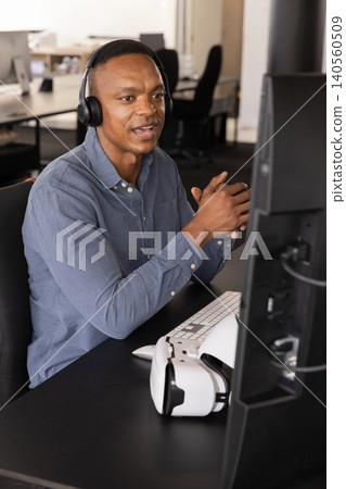 African american man explaining data analysis at office desk with computer monitor, vr headset 140560509