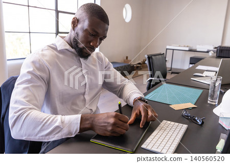 African american man in white shirt sketching on tablet near hard hat at office desk African american man in white shirt sketching on tablet near hard hat at office desk 140560520