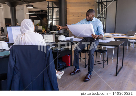 Diverse architects working on blueprint at open-plan office desk with laptop, copy space 140560521