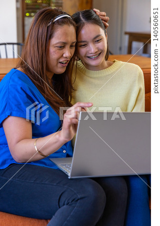Asian mother and teenage daughter sitting on sofa in living room using laptop computer Asian mother and teenage daughter sitting on sofa in living room using laptop computer 140560651