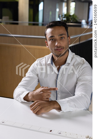 Asian man in white shirt pointing at forearm while sitting at office desk with power outlet Asian man in white shirt pointing at forearm while sitting at office desk with power outlet 140560699