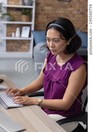 Asian woman typing on white keyboard at wood desk in office with laptop and smartphone 140560759