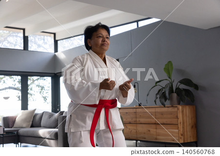 Senior indian woman practicing martial arts stance in living room wearing white gi and belt Senior indian woman practicing martial arts stance in living room wearing white gi and belt 140560768