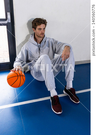Male sitting on gym floor wearing tracksuit and whistle while holding basketball 140560776