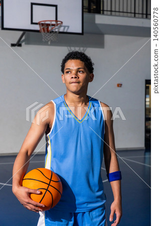 Teenage boy wearing wristband standing on court holding basketball by line near backboard hoop Teenage boy wearing wristband standing on court holding basketball by line near backboard hoop 140560778