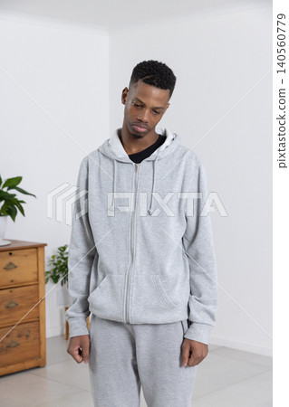 African american man standing near room corner in sportswear by wooden chest and plant African american man standing near room corner in sportswear by wooden chest and plant 140560779