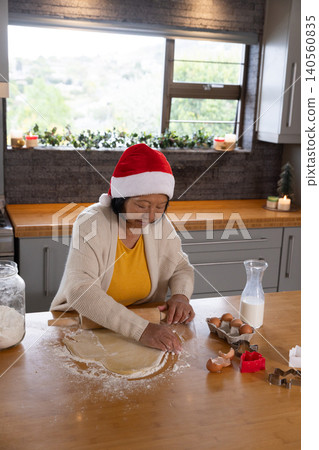 Senior Asian woman in Santa hat rolling cookie dough on home kitchen countertop with rolling pin Senior Asian woman in Santa hat rolling cookie dough on home kitchen countertop with rolling pin 140560835