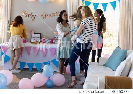 Female friends holding infant, offering toy, arranging cupcakes, gift bags in living room Female friends holding infant, offering toy, arranging cupcakes, gift bags in living room 140560874
