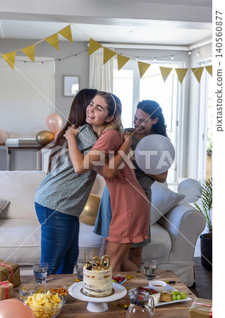 Three female friends hugging and celebrating 30th birthday in living room with cake, balloons 140560877