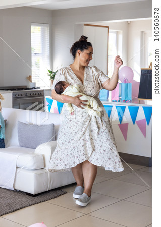 Mother with two children holding newborn and reaching for balloon in living room next to kitchen 140560878