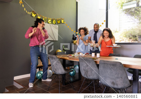 Diverse friends standing around dining table at home, food platters balloons welcome banner 140560881