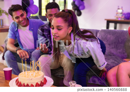 Diverse teenage friends celebrating around cake on coffee table at home under balloons Diverse teenage friends celebrating around cake on coffee table at home under balloons 140560888