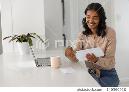 Woman sorting mail at white kitchen island with laptop mug plant, copy space Woman sorting mail at white kitchen island with laptop mug plant, copy space 140560918