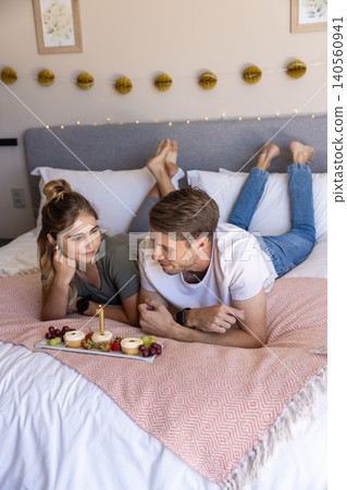 Couple lying on peach blanket on king-size bed pointing at frosted cupcakes on wooden tray Couple lying on peach blanket on king-size bed pointing at frosted cupcakes on wooden tray 140560941