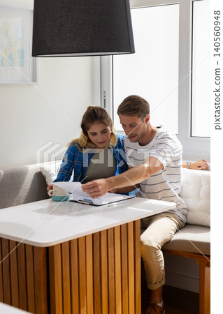 Couple reviewing papers on clipboard while sitting at wooden table in dining nook with coffee mug Couple reviewing papers on clipboard while sitting at wooden table in dining nook with coffee mug 140560948