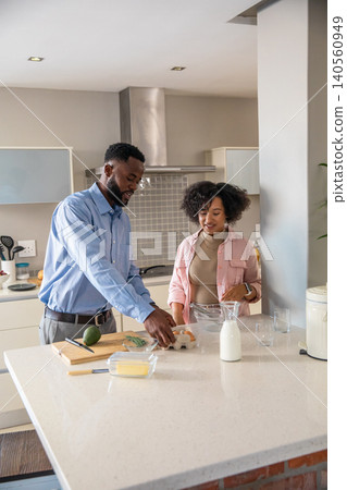 Diverse couple grabbing eggs and pouring milk from bottle, chopping avocado at kitchen island Diverse couple grabbing eggs and pouring milk from bottle, chopping avocado at kitchen island 140560949