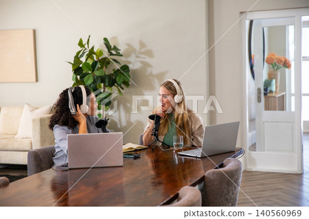 Diverse female friends recording podcast on laptops with microphones, headphones in living room Diverse female friends recording podcast on laptops with microphones, headphones in living room 140560969