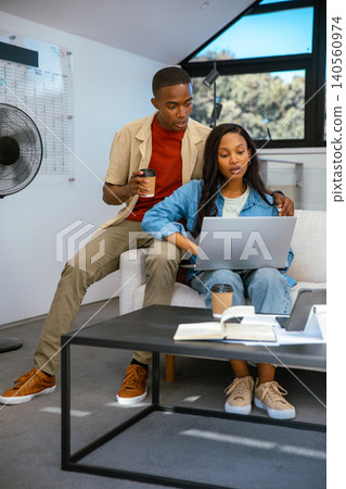 African American couple sipping coffee and working on laptop in office with planning chart notebook African American couple sipping coffee and working on laptop in office with planning chart notebook 140560974