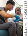 Hispanic caregiver holding senior patient hand, preparing finger-prick wearing gloves 140561136