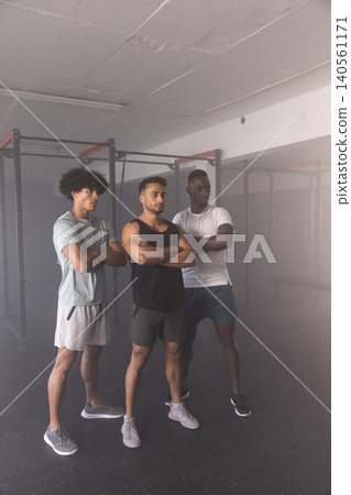 Diverse male workout partners standing with arms crossed in gym before pull-up and squat rack 140561171