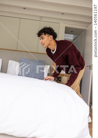 Hispanic male wearing sweater and trousers making king-size bed in bedroom, copy space Hispanic male wearing sweater and trousers making king-size bed in bedroom, copy space 140561197