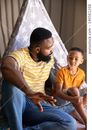 African American father and son talking inside gray-and-white teepee with cushions in playroom African American father and son talking inside gray-and-white teepee with cushions in playroom 140561208