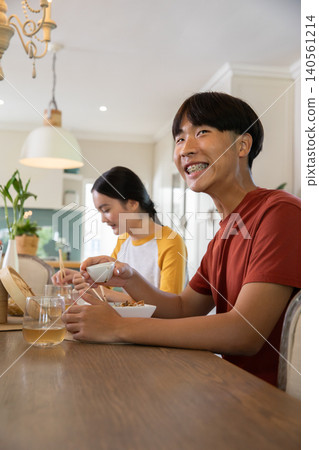 Asian friends eating dinner in home kitchen at dining table with chopsticks, bowls, steamer Asian friends eating dinner in home kitchen at dining table with chopsticks, bowls, steamer 140561214