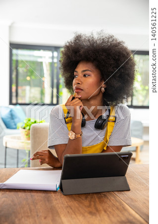 African american woman sitting at table at home holding pen, notebook and tablet African american woman sitting at table at home holding pen, notebook and tablet 140561225