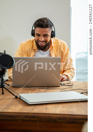 Smiling man in shirt sitting at home workspace recording on laptop with microphone Smiling man in shirt sitting at home workspace recording on laptop with microphone 140561227