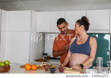 Diverse couple slicing fruit on cutting board at kitchen island, berry bowls, baby bump, copy space Diverse couple slicing fruit on cutting board at kitchen island, berry bowls, baby bump, copy space 140561257