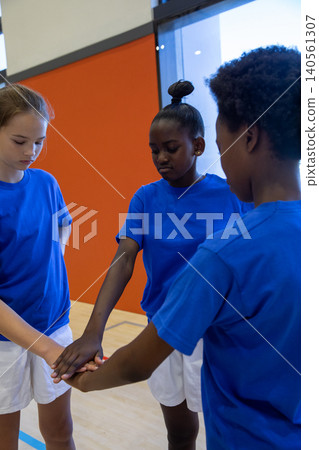 Diverse teen athletes stacking hands together in gym on floor wearing blue shirts and shorts Diverse teen athletes stacking hands together in gym on floor wearing blue shirts and shorts 140561307